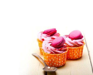 Fresh pink berry cream cupcake with macaroon on top over rustic wood table