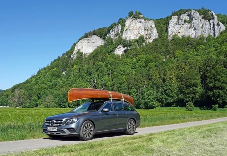 Mercedes with cedar wood canoe on roof in front of rocks in the Danube valley