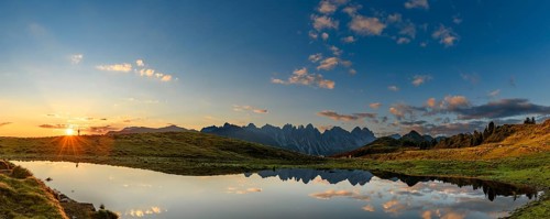 Salfainsee with reflection of the Kalkkoegel and mountaineers on mountain meadow at sunrise