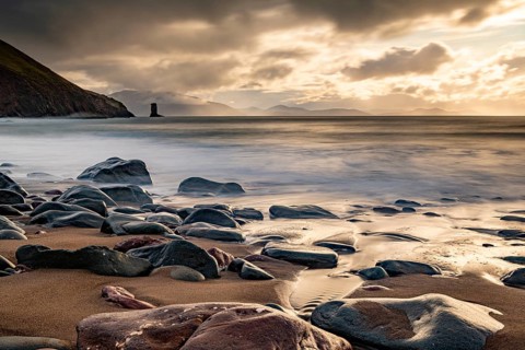 Sandy beach beach with stones on North Atlantic with rocky outcrop and cloudy sky