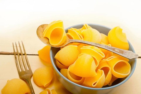 Raw Italian snail lumaconi pasta on a blue bowl over rustic table macro