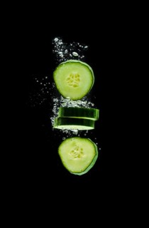 Sliced bio cucumber splashing water isolated on black background