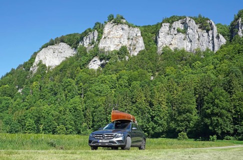 Mercedes with cedar wood canoe on roof in front of rocks in the Danube valley