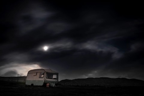 Old caravan in meadow under full moon