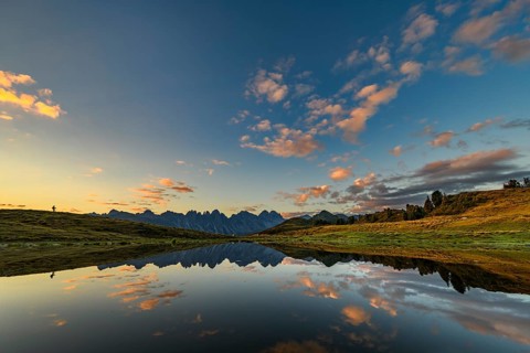 Salfainsee with reflection of the Kalkkoegel and mountaineers on mountain meadow at sunrise
