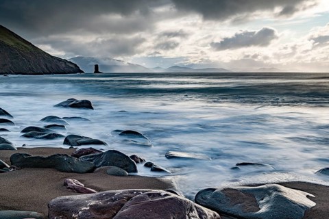 Sandy beach beach with stones on North Atlantic with rocky outcrop and cloudy sky