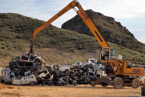 Crane piles scrap car on top of other cars