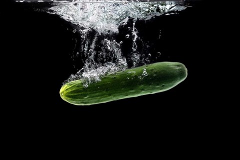 Whole bio cucumber sinking under water against black background