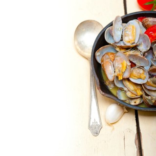 Fresh clams stewed on an iron skillet over wite rustic wood table