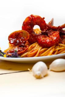 Italian seafood spaghetti pasta on red tomato sauce over white rustic wood table