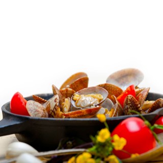 Fresh clams stewed on an iron skillet over wite rustic wood table