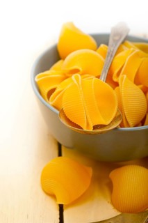 Raw Italian snail lumaconi pasta on a blue bowl over rustic table macro
