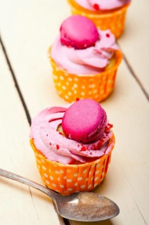 Fresh pink berry cream cupcake with macaroon on top over rustic wood table