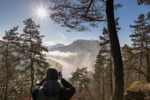 Man taking a photo of the view from the Biedermann Mausoleum into the Elbe Valley with Koenigstein Fortress in the morning mist