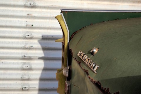 Rear end of old Peugeot in front of corrugated sheet metal