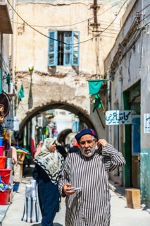 An elderly man in traditional attire walking through the streets of the old town of Tripoli