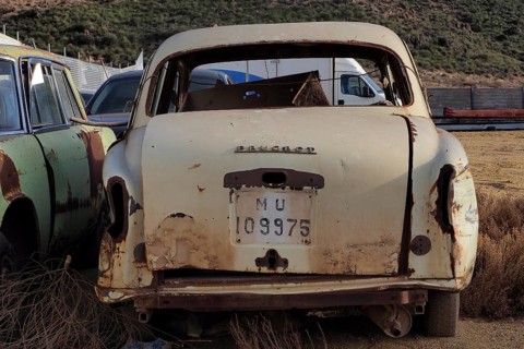 Rear view of beige scrapped Peugeot with painted number plate