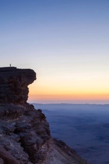 Alone figure on top of the cliffs overlooking the majestic desert of Makhtesh Ramon