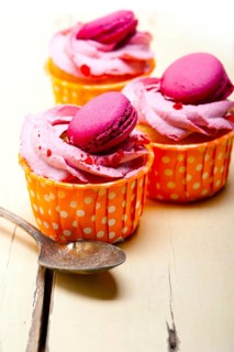 Fresh pink berry cream cupcake with macaroon on top over rustic wood table