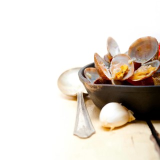 Fresh clams stewed on an iron skillet over wite rustic wood table