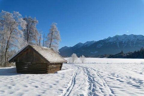 Winter landscape with snowshoe trails and haystack near frozen lake Barmsee