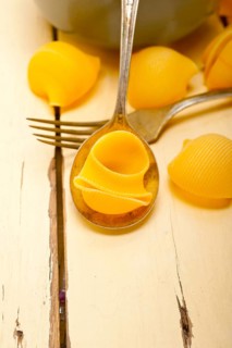 Raw Italian snail lumaconi pasta on a blue bowl over rustic table macro
