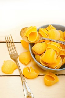 Raw Italian snail lumaconi pasta on a blue bowl over rustic table macro