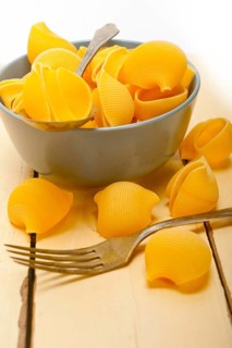 Raw Italian snail lumaconi pasta on a blue bowl over rustic table macro