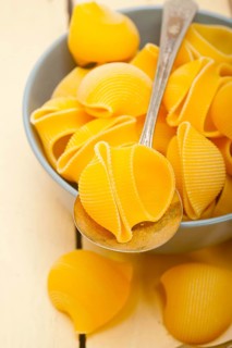 Raw Italian snail lumaconi pasta on a blue bowl over rustic table macro