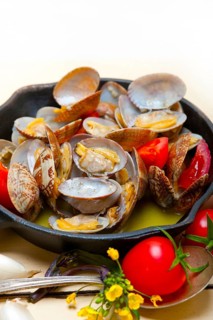 Fresh clams stewed on an iron skillet over wite rustic wood table