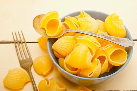 Raw Italian snail lumaconi pasta on a blue bowl over rustic table macro