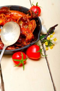 Fresh seafood stew prepared on an iron skillet ove white rustic wood table