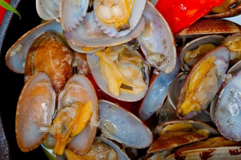 Fresh clams stewed on an iron skillet over wite rustic wood table