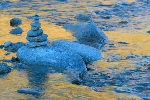 Stack of stones on mountain stream with reflecting larches in the water