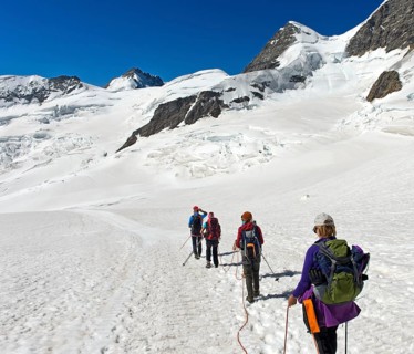 Mountain guide with alpinists on rope crossing the Jungfraufirn