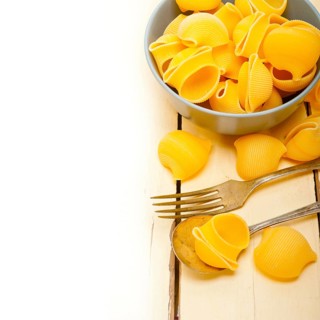 Raw Italian snail lumaconi pasta on a blue bowl over rustic table macro