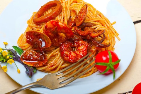 Italian seafood spaghetti pasta on red tomato sauce over white rustic wood table