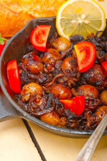 Baby cuttle fish roasted on iron skillet with tomatoes and onions over rustic wood table