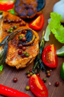 Wood fired hoven cooked chicken breast on wood board with herbs spices and vegetables