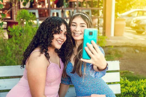 Two pretty girls sitting on a bench taking a selfie