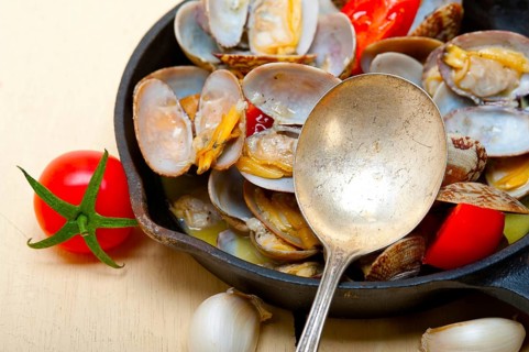 Fresh clams stewed on an iron skillet over wite rustic wood table