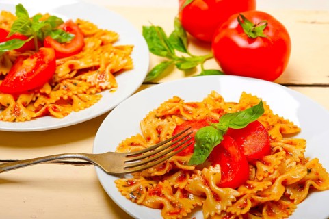 Italian pasta farfalle butterfly bow-tie with tomato basil sauce over white rustic wood table