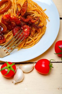 Italian seafood spaghetti pasta on red tomato sauce over white rustic wood table