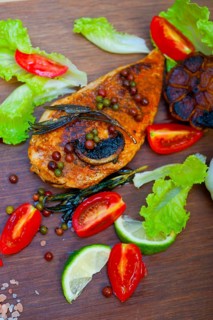Wood fired hoven cooked chicken breast on wood board with herbs spices and vegetables