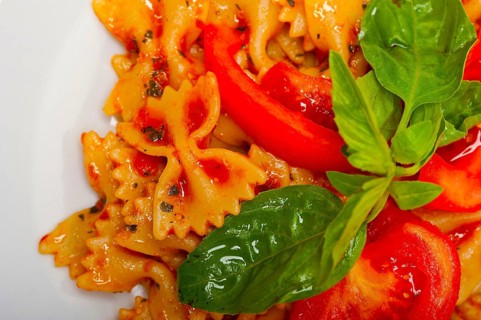 Italian pasta farfalle butterfly bow-tie with tomato basil sauce over white rustic wood table