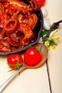 Fresh seafood stew prepared on an iron skillet ove white rustic wood table
