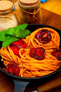 Italian spaghetti pasta and tomato with mint leaves on iron skillet over wood board