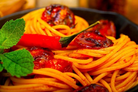 Italian spaghetti pasta and tomato with mint leaves on iron skillet over wood board