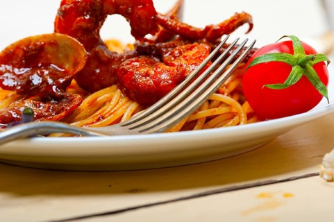 Italian seafood spaghetti pasta on red tomato sauce over white rustic wood table