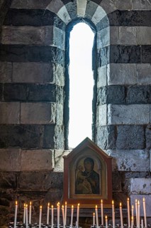 Burning candles in front of an image of the Virgin Mary in front of an open window of the church of San Pietro